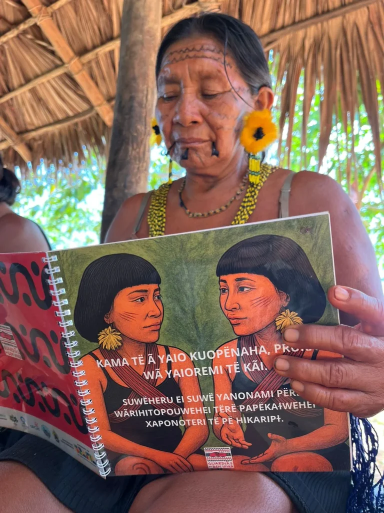 A Yanomami woman holding an illustrated booklet written in the Yanomami language