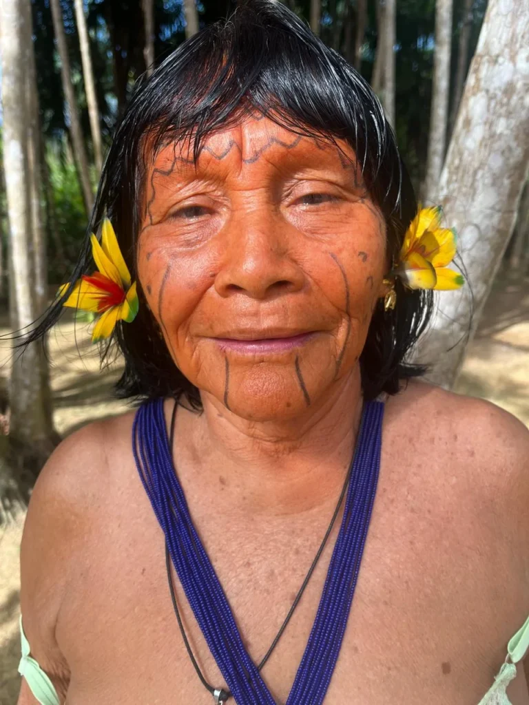 Portrait of a smiling Yanomami elder with yellow flowers in her ears and a blue bead necklace